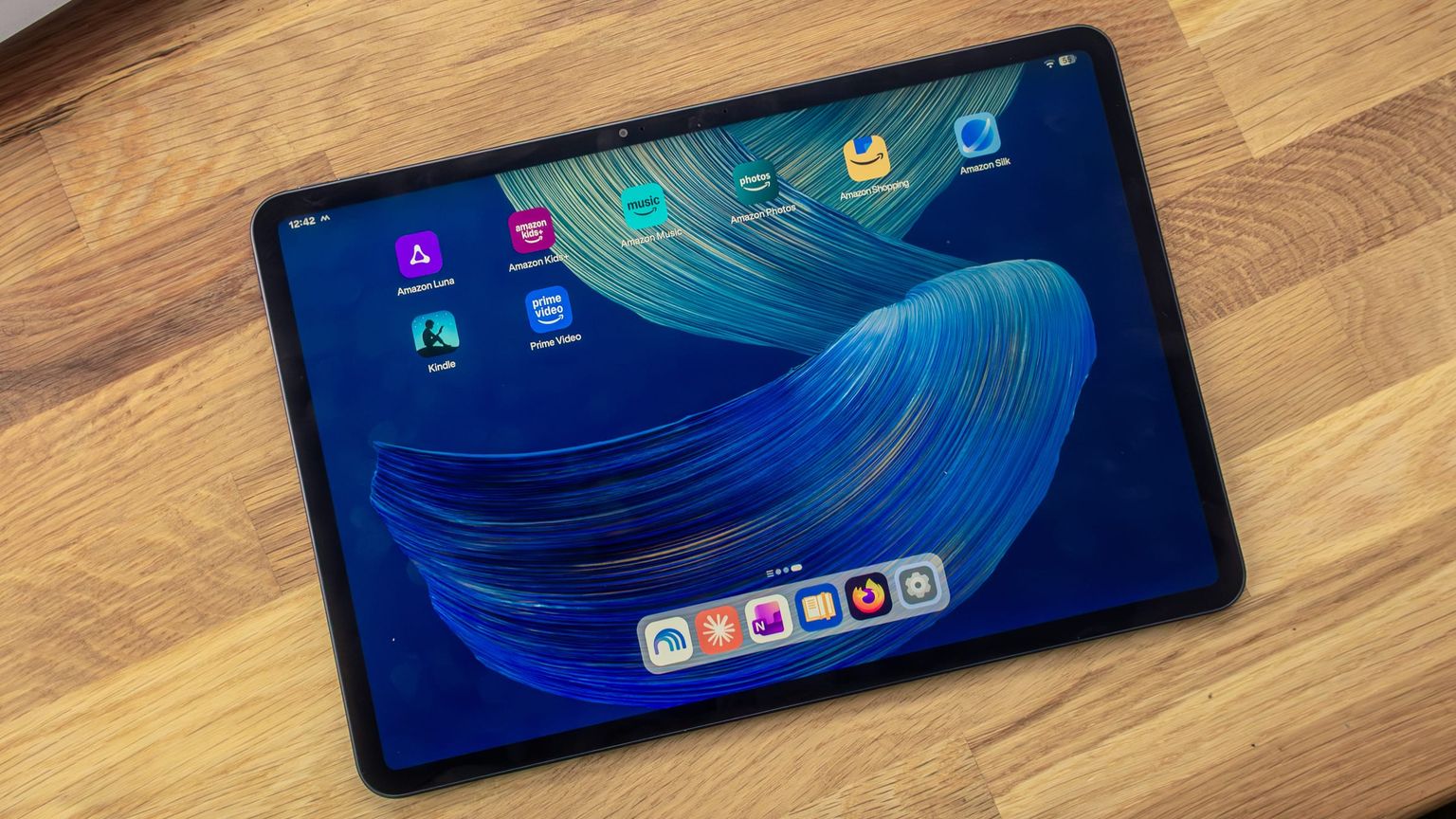 Alexa Tablet 12 Pro auf einem Holztisch, Startbildschirm mit den vorinstallierten Amazon-Apps und einem Dock mit sechs Apps