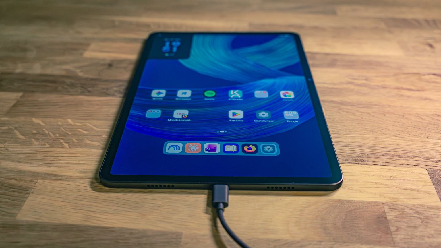 Alexa Tablet 12 Pro mit aufgeräumtem Startbildschirm und angeschlossenem USB-C-Kabel auf einem Holztisch