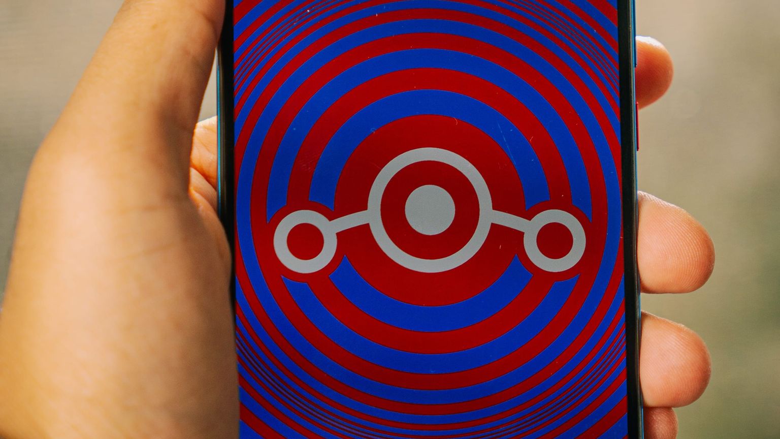 Smartphone in der Hand, auf dem Display das LineageOS-Logo vor roten und blauen Ringen